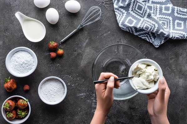 Partial view of woman putting sour cream into bowl while making cream for pie on dark grey surface — Stock Photo