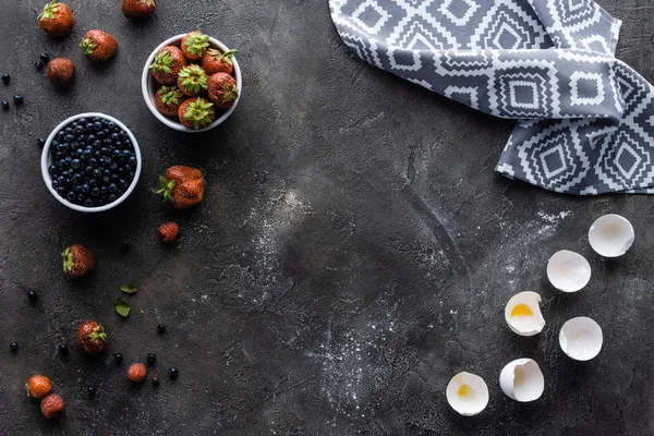 Flat lay with fresh berries, eggshells and linen in dark grey surface — Stock Photo