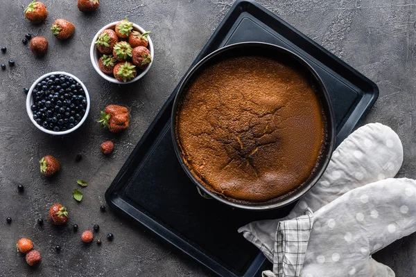 Flat lay com torta caseira assada, bagas frescas e pano de forno em mesa cinza escuro — Fotografia de Stock