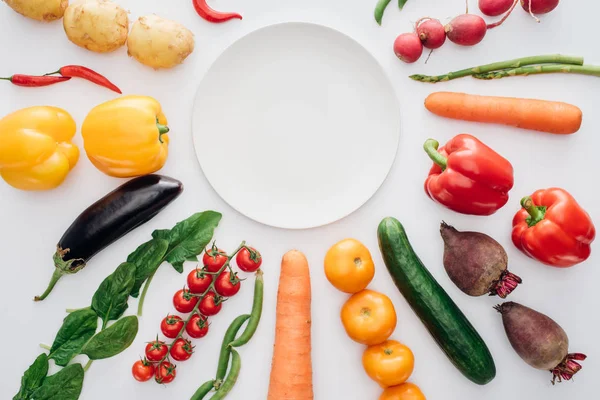 Вид сверху на пустую круглую тарелку и свежие органические овощи, изолированные на белом — стоковое фото