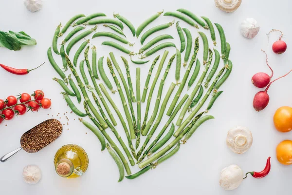 Vista superior del corazón hecho de guisantes verdes frescos y verduras maduras aisladas en blanco - foto de stock