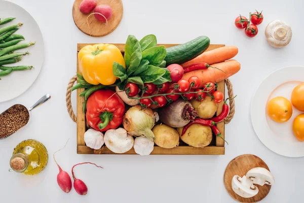 Вид сверху коробки со свежими овощами и тарелками, изолированными на белом — стоковое фото