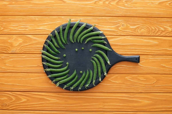 Vue de dessus des pois verts frais sur la planche ronde sur le dessus de table en bois — Photo de stock