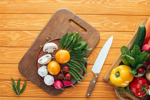 Top view of fresh raw healthy vegetables in box and in plate on wooden cutting board — Stock Photo