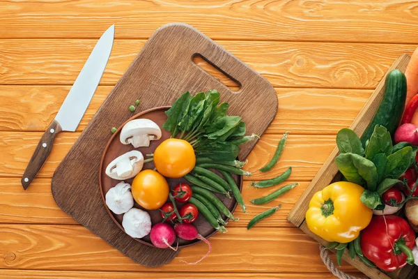 Vue du dessus des légumes crus frais en boîte et en assiette sur planche à découper en bois — Photo de stock