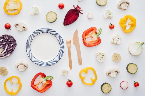 Vista superior de la placa redonda vacía, tenedor de madera con cuchillo y verduras frescas en rodajas aisladas en blanco - foto de stock