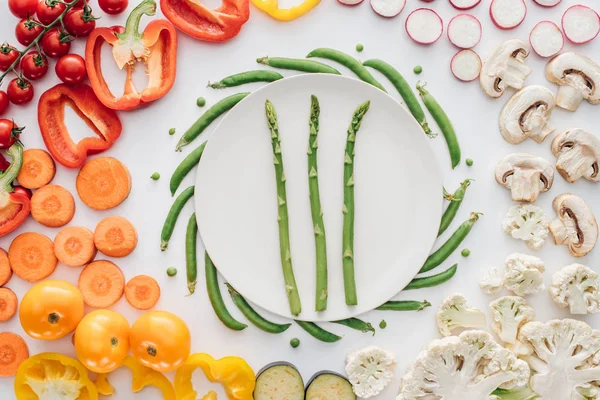 Vista dall'alto di asparagi freschi su piatto bianco rotondo e verdure biologiche isolate su bianco — Foto stock
