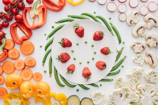 Vue de dessus des fraises fraîches mûres et des pois verts sur plaque ronde blanche et légumes biologiques isolés sur blanc — Photo de stock