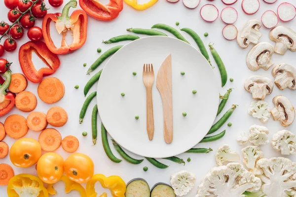 Top view of wooden fork and knife on round white plate and fresh organic vegetables isolated on white — Stock Photo