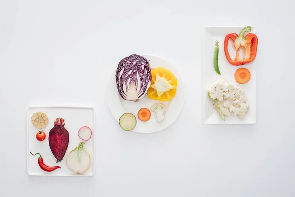 Vista superior de vegetais frescos crus saudáveis em placas brancas isoladas em branco — Fotografia de Stock