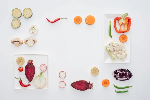 Вид зверху на квадратні білі тарілки і свіжі нарізані овочі ізольовані на білому — стокове фото