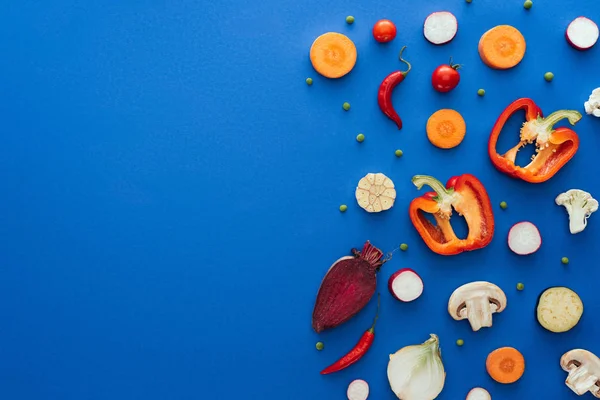 Vista superior de verduras crudas en rodajas sobre fondo azul - foto de stock