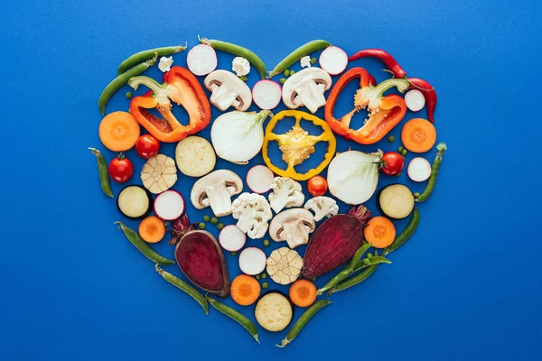 Top view of various raw healthy vegetables in shape of heart isolated on blue — Stock Photo