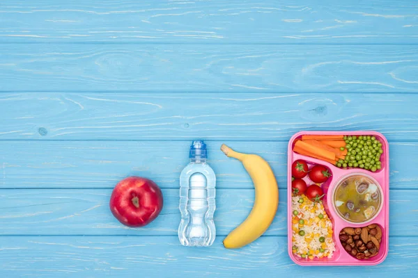 Vista elevada de la bandeja con almuerzo para niños para la escuela, botella de agua y frutas en la mesa azul — Stock Photo