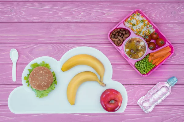 Vista superior de la bandeja con almuerzo para niños para la escuela, hamburguesa y frutas en la mesa rosa — Stock Photo