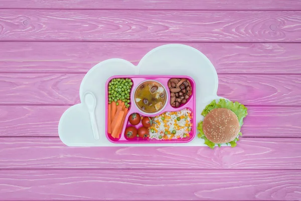 Top view of tray with kids lunch for school and burger on pink table — Stock Photo