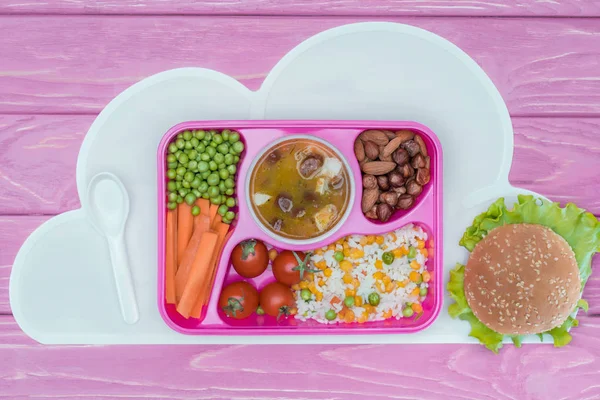 Вид на поднос с детским обедом для школы и бургером на розовом столе — стоковое фото