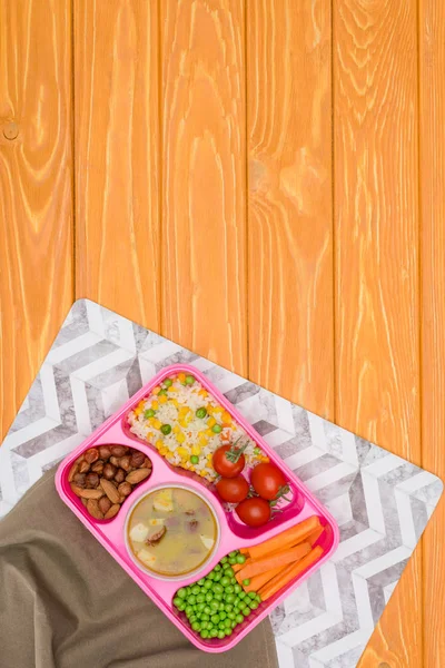 Vista superior de la bandeja con almuerzo para niños para la escuela con servilletas en mesa de madera naranja - foto de stock