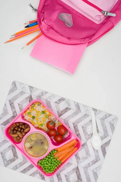 Vue du dessus du plateau avec des enfants déjeuner pour l'école et sac rose avec crayons sur table blanche — Photo de stock
