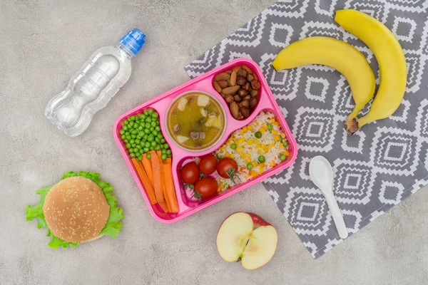 Vista superior de la bandeja con almuerzo para niños para la escuela y frutas en servilleta sobre mesa de mármol - foto de stock
