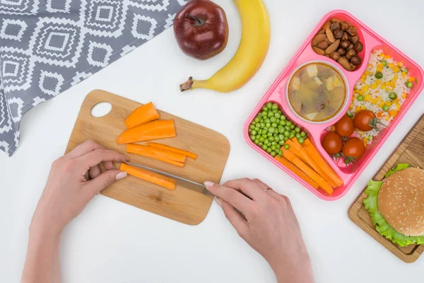 Zugeschnittenes Bild einer Mutter, die Kindern das Abendessen für die Schule bereitet und Möhren schneidet — Stockfoto