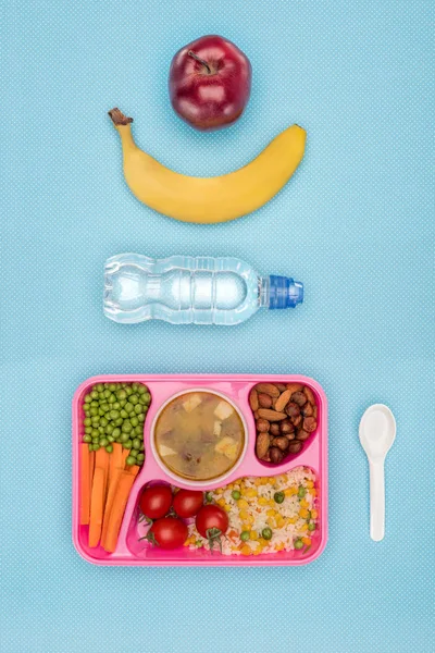 Top view of tray with kids lunch for school, bottle of water, banana and apple on blue surface — Stock Photo