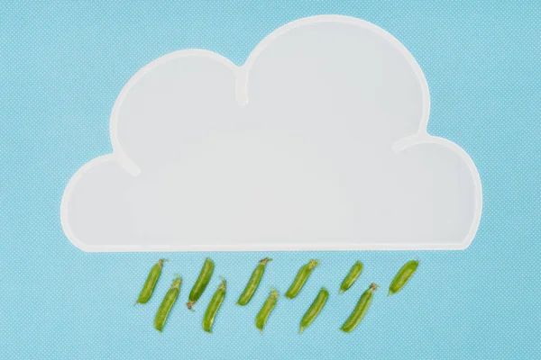 Top view of white napkin in shape of cloud with rain of pea pods isolated on blue — Stock Photo