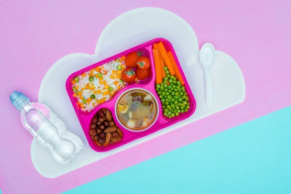 Draufsicht auf Tablett mit Mittagessen für die Schule und Flasche Wasser auf violettem und blauem Tisch — Stockfoto