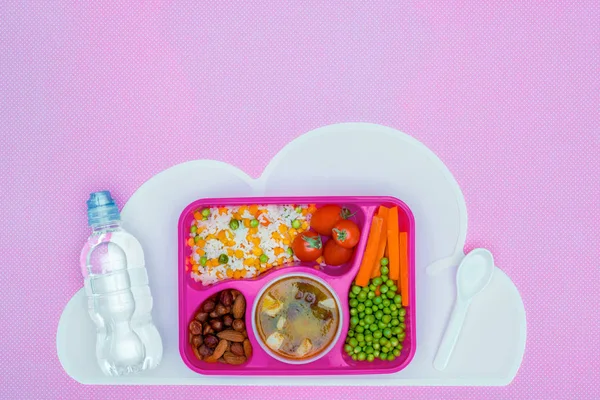 Draufsicht auf Tablett mit Mittagessen für Schulkinder, Flasche Wasser und Plastiklöffel auf violettem Tisch — Stockfoto