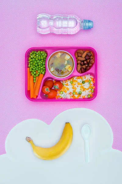 Top view of tray with kids lunch for school, bottle of water and banana on violet table — Stock Photo
