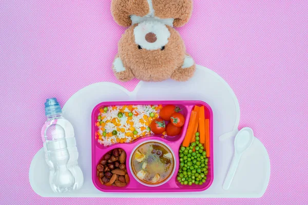 Вид зверху лоток з дітьми обід для школи і плюшевий ведмідь на фіолетовій поверхні — стокове фото