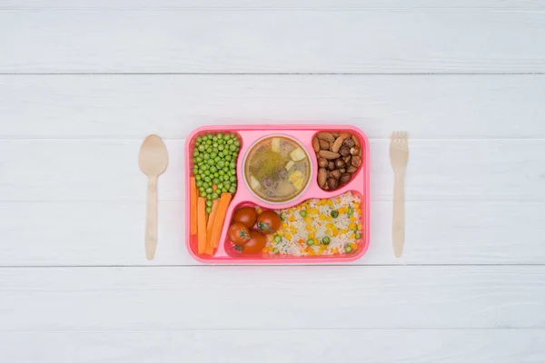 Vista superior de la bandeja con almuerzo para niños para la escuela y cuchara de madera y tenedor en la mesa - foto de stock