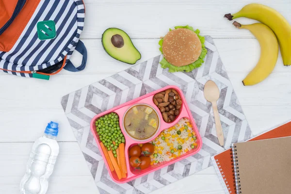 Vista superior de la bandeja con almuerzo para niños para la escuela y copybooks en mesa de madera - foto de stock