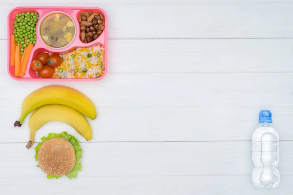 Vista superior da bandeja com crianças almoço para a escola, bananas e garrafa de plástico de água na mesa branca — Fotografia de Stock