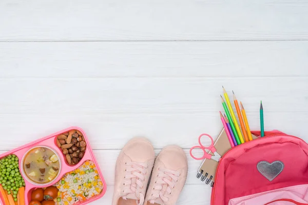 Vue du dessus du plateau avec déjeuner pour enfants, sac d'école avec crayons et chaussures sur surface blanche — Photo de stock