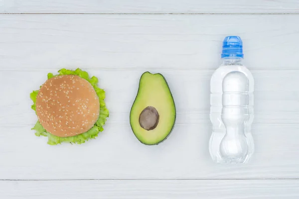 Draufsicht auf Burger, Avocado und Plastikflasche mit Wasser auf Holztisch — Stockfoto