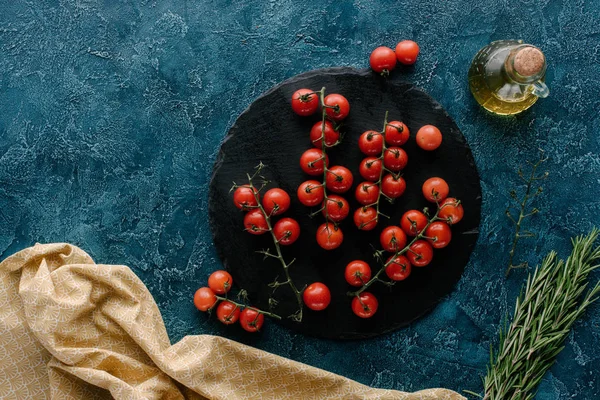 Placa de ardósia escura com tomate cereja e garrafa de óleo na mesa azul — Fotografia de Stock