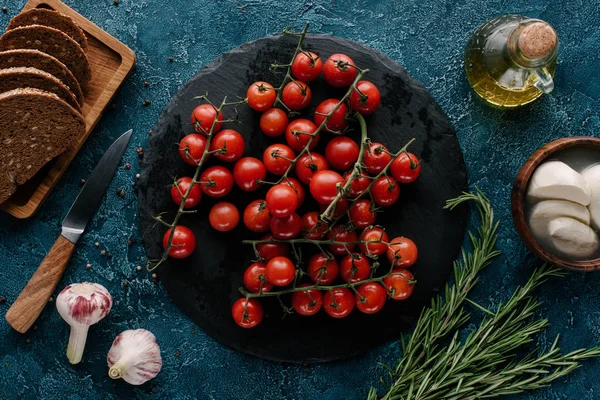 Pizarra oscura con tomates rojos en la mesa azul con pan y condimentos - foto de stock