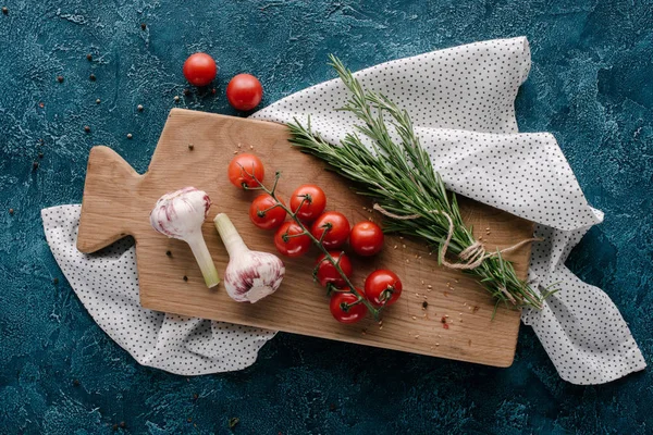 Wooden board with tomatoes and garlic on dark blue table — Stock Photo