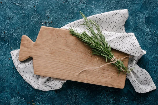 Placa de corte de madeira com erva de alecrim na mesa azul escura — Fotografia de Stock