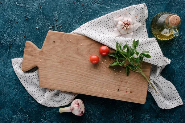 Planche à découper avec tomates et basilic sur table bleu foncé — Photo de stock