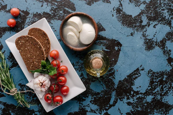 Teller mit Tomaten und Brot auf dunkelblauem Tisch mit Mozzarella und Öl — Stockfoto