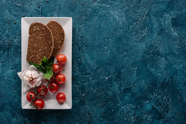 Placa con trozo de pan y tomates rojos sobre mesa oscura - foto de stock