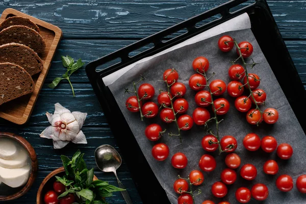 Red cherry tomatoes in baking on dark wooden table by condiments and bread — Stock Photo