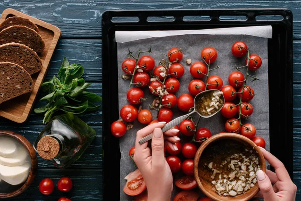 Abgeschnittene Ansicht weiblicher Hände, die Knoblauchöl auf Kirschtomaten in Backform gießen — Stockfoto