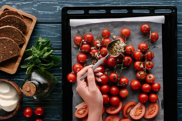 Mujer vertiendo salsa de ajo en los tomates en la bandeja de hornear por ingredientes de cocina - foto de stock