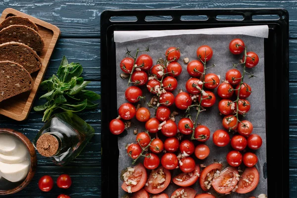 Tomates cereja assados com alho e queijo na mesa de madeira escura com pão e óleo — Fotografia de Stock