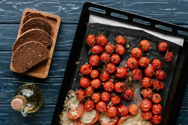 Tomates rojos cereza al horno con queso sobre mesa de madera oscura con pan y aceite - foto de stock