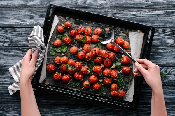 Woman pouring sauce on baked tomatoes in pan on dark wooden table — Stock Photo