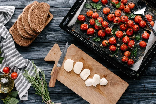 Pieces of bread and mozzarella on dark wooden table with tomatoes in baking pan — Stock Photo